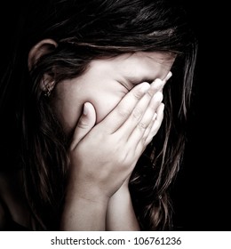 Grunge close-up portrait of a girl crying and covering her face isolated on black