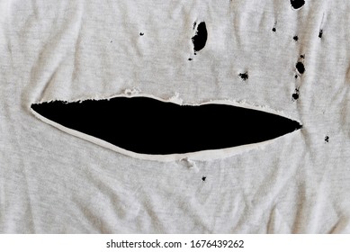 Grunge damaged cloth on black background. Gray white fabric with holes. Texture of an old dirty ragged t shirt. Crumpled torn rag. Copy space