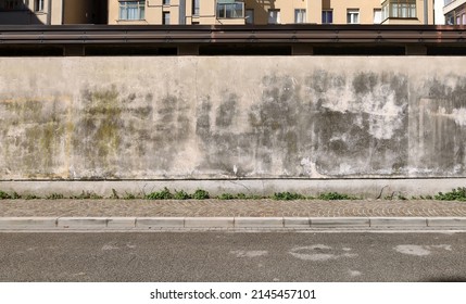 Grunge plaster wall  with moss and stains. Sidewalk and asphalt road in front. Background for copy space. - Shutterstock ID 2145457101