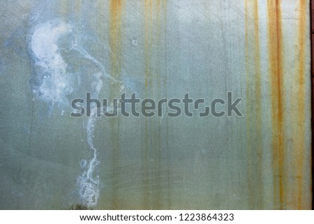 Grungey blue-grey metal sheet with stained rusting orange lines running down from the top and white paint splash