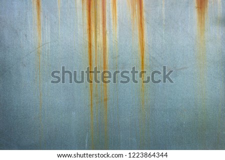 Grungey blue-grey metal sheet with stained rusting orange lines running down from the top