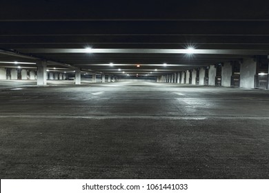Grungy, dimly lit empty parking garage with overhead lights and an exit sign hanging from the ceiling. - Shutterstock ID 1061441033