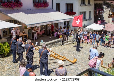 Gruyere, Switzerland - July 29.2021: A Swiss musician group play the traditioanl music instrument alphorn with a flag bearer to swing the National flag at Gruyere village as a tourist attraction.

