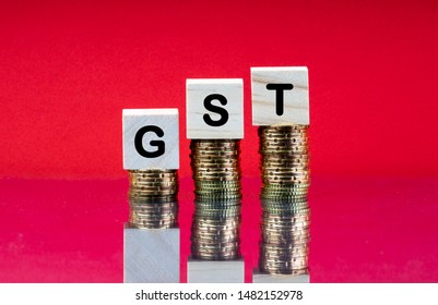 GST Or TAX Concept With Wooden Block On Stacked Coins And Red Background