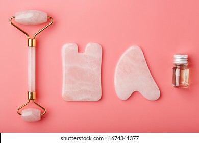 Gua sha massage tool made of natural pink Quartz-roller, jade stone and oil, on a pink background for face and body care. Part of traditional Chinese medicine