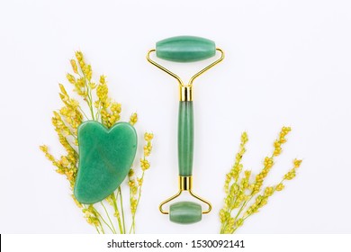 Gua sha stone and jade roller still life arranged with golden wildflowers on white surface / natural holistic beauty concept