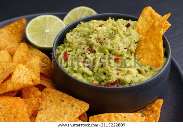 Guacamole dip with tortilla chips or nachos in\
black plate on a black\
background