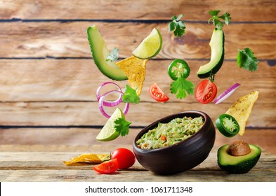 Guacamole with flying corn chips and ingredients to prepare it on a wood background. toning. selective focus