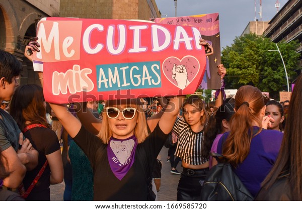 Guadalajara, Mexico -\
03 08 2020: Young blonde woman wearing sunglasses holds up a sign\
reading \