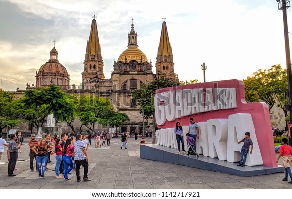 Guadalajara, Mexico - June 26, 2018: Tourist\
gather in Liberation Square and pose for photos by the sign in\
front of the Guadalajara\
Cathedral.