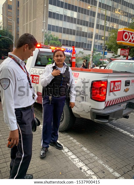 Guadalajara, Mexico -\
October 19 2019:  Male and female traffic police officers on duty\
standing on the street by official police vehicle, wearing white\
and blue police uniform \
