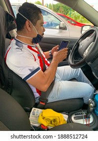 Guadalajara, Mexico; October 25 2020: Adult Hispanic Mexican Male Uber Driver Sits On Car Waiting For Next Trip. Male Sits On Driver's Seat In Parked Car. Chivas Soccer Uniform Shirt