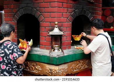 Guan Di Chinese Taoist Temple. Man And Woman Burning Joss Paper Offerings In Kiln.  Kuala Lumpur. Malaysia.  12-20-2019