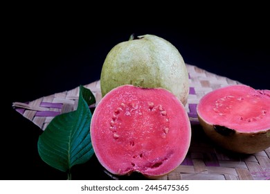 Guava isolated. Collection of red fleshed guava fruit with yellowish green skin and leaves isolated on black background with woven bamboo.