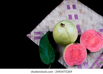 Guava isolated. Collection of red fleshed guava fruit with yellowish green skin and leaves isolated on black background with woven bamboo.