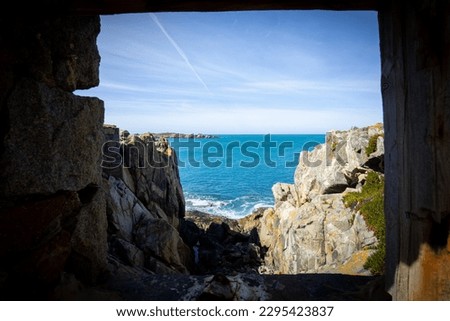 Guernsey coastline, a view of the rocky shore and bright blue sea through a window in an old military fortress. 