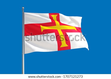 Guernsey national flag waving in the wind on a deep blue sky. High quality fabric. International relations concept.