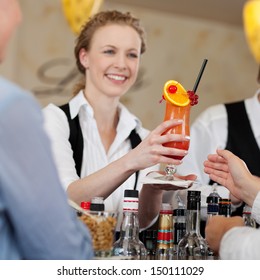 Guest being served a colourful orange and rum tropical cocktail by a smiling barmaid in a hotel or restaurant