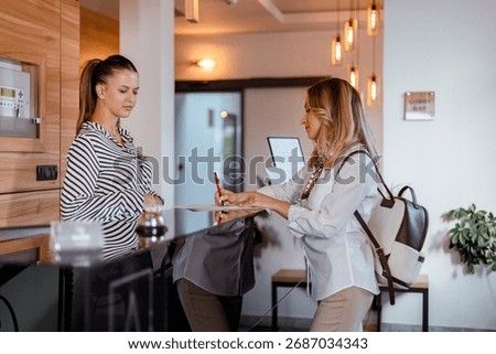 A guest is checking in at the hotel reception while the receptionist provides assistance and information. The setting is bright and welcoming.