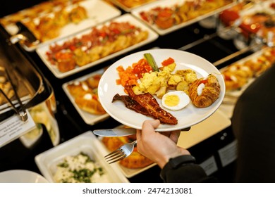 Guest picks up different food at the breakfast buffet at the hotel