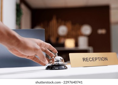 Guest ringing service bell at front desk, waiting to receive assistance from hotel staff at reception counter. Male tourist calling out receptionist, looking for accommodation. Close up.