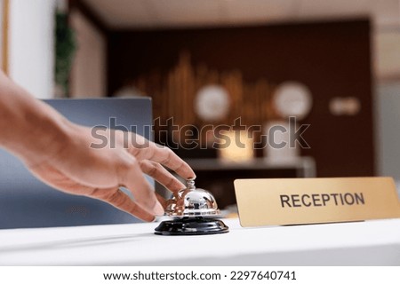 Guest ringing service bell at front desk, waiting to receive assistance from hotel staff at reception counter. Male tourist calling out receptionist, looking for accommodation. Close up.