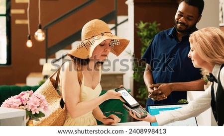 Guests doing mobile nfc payment on pos terminal in lobby, using smartphone and paying for room at tropical seaside hotel. Happy couple registering at exotic resort front desk area.