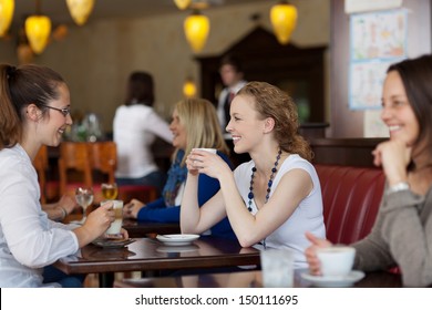 Guests enjoying coffee in a restaurant with focus to two stylish young woman sitting at a table together - Powered by Shutterstock