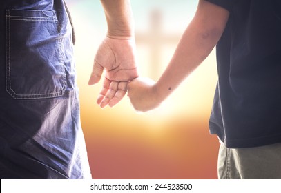 Guidance family concept: Child's hand holding father's finger on blurred cross on sunset background.