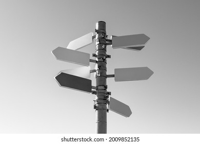 Guidepost with arrows in sunlight against sky background. Black and white photography.