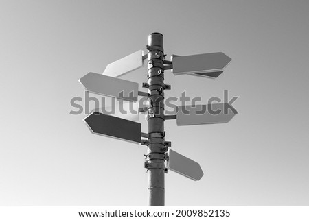 Guidepost with arrows in sunlight against sky background. Black and white photography.
