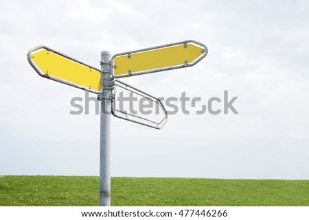 guidepost (three directions) in front of a green north sea dike