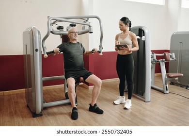 Guiding Senior Man Exercising on Chest Press Machine - Powered by Shutterstock