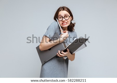 Guilty female nerd in funny eyeglasses which talking on phone and holding laptop, clipboard and notebook