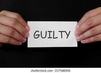 Guilty Verdict Concept. Criminal Hands Holding Paper Placard Mug Shot With Written Word In Dark Black Background.