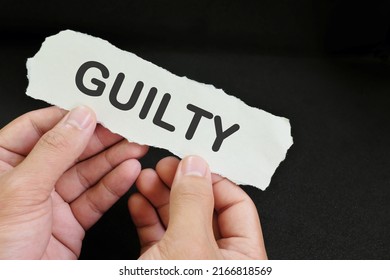 Guilty Verdict Concept. Hand Holding A Piece Of Paper With Written Word Guilty In Black Background.