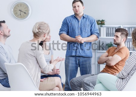 Guilty young man standing in an addiction therapy meeting and listening to psychologist
