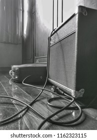 Guitar Amp And Power Lines. Guitar Case On The Wooden Floor Is Black And White.