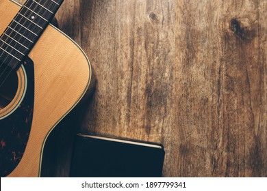 A guitar and a bible on a wooden background in a dimly lit environment