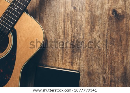 A guitar and a bible on a wooden background in a dimly lit environment