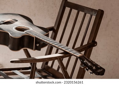 Guitar. Guitar chords. Acoustic guitar. Music. Musical background. An image of an acoustic guitar in a room with a retro armchair. Hard light. Shadows.