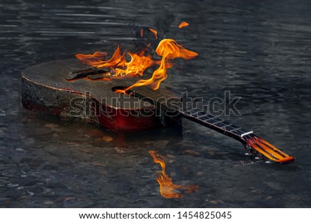 Guitar In Flames And Black Smoke Reflection In Water. Burning Guitar In River Water. Burning Musical Instrument On Dark Surface Of  Water. Concept Of Crisis Of Authorship.