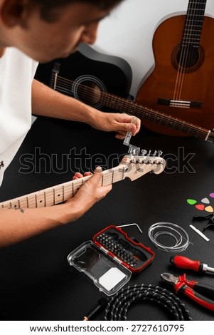 Guitar Maintenance and String Replacement. Guitar headstock being adjusted with a string winder. Guitar strings are tightened with a clear plastic winder on a polished headstock