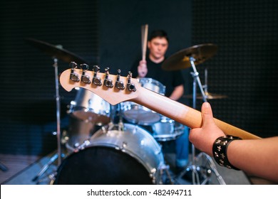 Guitar Neck Close-up On Drum Set Background . Focus On Guitar Neck And Guitar Player Hand, Drummer Playing On Drums On Background. Alive Performance