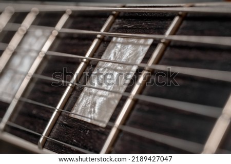 Guitar neck fretboard or fingerboard close up of frets and strings. The neck is bound and the rosewood fretboard features mother of pearl style block inlays