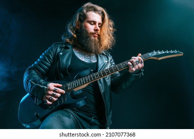 Guitar Player. Rockstar Bearded Man With Long Hair Plays On Electric Guitar Isolated On Smoke Black Background. Studio Shot 