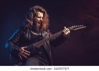 Guitar Player. Rockstar Bearded Man With Long Hair Emotional Plays On Guitar Isolated On Black Background. Studio Shot 