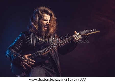 Guitar player. Rockstar bearded man with long hair emotional plays on guitar isolated on black background. Studio shot 