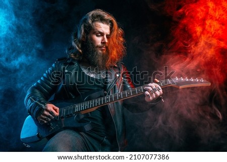 Guitar player. Rockstar bearded man with long hair plays on guitar isolated on smoke background. Studio shot 
