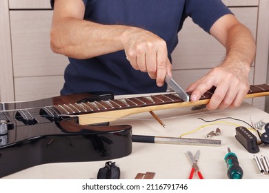Guitar repairman crowning frets on the guitar neck with fret files.